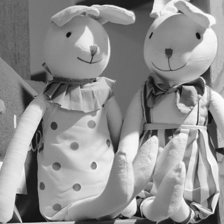 Zwei Stoffhasen mit Latzkleidern und Schlappohren im Retro-Stil.