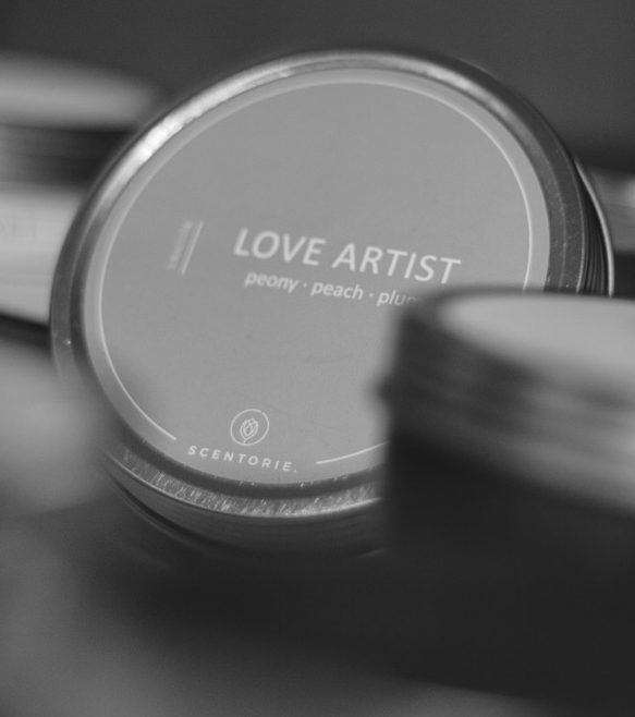 Kerzendose mit der Aufschrift "LOVE ARTIST", unscharf im Hintergrund.