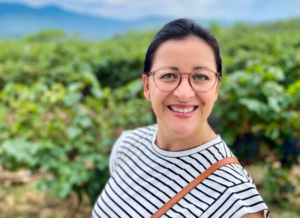 Frau mit Brille und gestreiftem Oberteil, lächelt vor unscharfem Hintergrund.